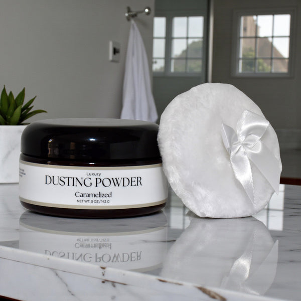 Jar of 'Luxury Dusting Powder' and a white powder puff on a marble surface with a blurred bathroom background.