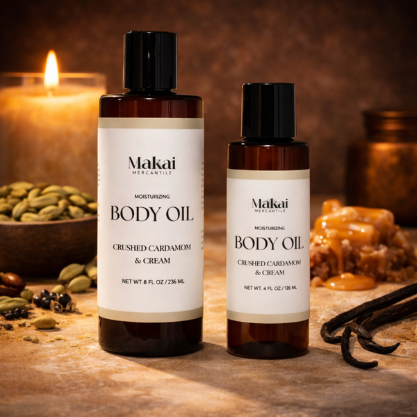 Two bottles of Makai Mercantile body oil on a wooden surface with spices and vanilla beans in Crushed Cardamom & Cream scent