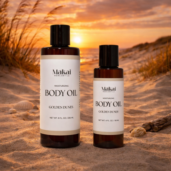 Two bottles of Makai Body Oil on sand with a sunset background depicting the warm and sweet scent of this fragrance.