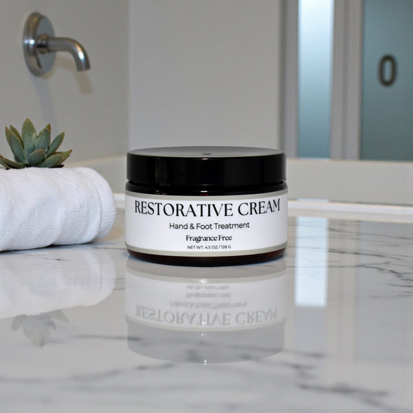Jar of Restorative Cream on a bathroom counter with towels and a plant in the background