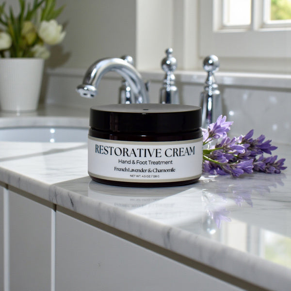 Restorative Cream jar on a marble countertop with lavender flowers and a sink in the background
