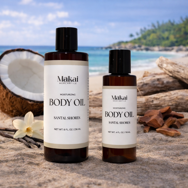Two bottles of Makai Mercantile body oil on a beach with a coconut, sandalwood and vanilla, and wood logs in the background. In the scent of Santal Shores.