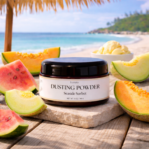 Dusting powder jar labeled 'Luxury Dusting Powder Seaside Sorbet' on a beach setting with fruits.